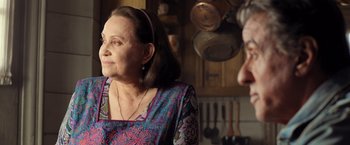 Movie still from “Rambo: Last Blood” (2019), directed by Adrian Grunberg – An older woman in a colorful dress in a kitchen; Close Up shot, Over the shoulder angle