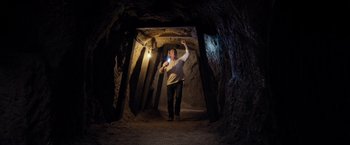 Movie still from “Rambo: Last Blood” (2019), directed by Adrian Grunberg – A man standing inside of a cave holding a flashlight; Wide shot, Low angle