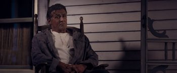 Movie still from “Rambo: Last Blood” (2019), directed by Adrian Grunberg – A man sitting in a chair with a knife in his hand; Medium shot, Low angle
