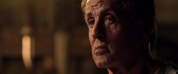 Movie still from “Rambo: Last Blood” (2019), directed by Adrian Grunberg – An older man looking into the distance in a dark room; Close Up shot, Over the shoulder angle