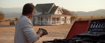 Movie still from “Rambo: Last Blood” (2019), directed by Adrian Grunberg – A man is holding something out of his trunk in front of a house; Wide shot, Low angle