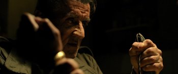 Movie still from “Rambo: Last Blood” (2019), directed by Adrian Grunberg – An older man looking at the camera while holding a cell phone; Close Up shot, Over the shoulder angle