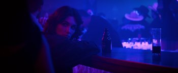 Movie still from “Rambo: Last Blood” (2019), directed by Adrian Grunberg – A woman sitting at a table with a bottle of beer in front of her; Close Up shot, Over the shoulder angle