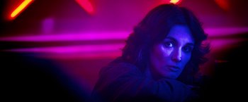 Movie still from “Rambo: Last Blood” (2019), directed by Adrian Grunberg – A woman in a purple room with lights in the background; Close Up shot, Over the shoulder angle