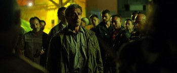 Movie still from “Rambo: Last Blood” (2019), directed by Adrian Grunberg – A group of men standing next to each other on a street; Medium shot, Over the shoulder angle