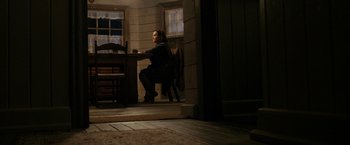 Movie still from “Rambo: Last Blood” (2019), directed by Adrian Grunberg – A person sitting at a desk in a room; Wide shot, High angle