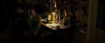 Movie still from “Rambo: Last Blood” (2019), directed by Adrian Grunberg – A man sitting at a desk with a lamp on top of it; Wide shot, High angle
