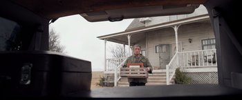 Movie still from “Rambo: Last Blood” (2019), directed by Adrian Grunberg – A man holding a crate in front of a house; Wide shot, Low angle
