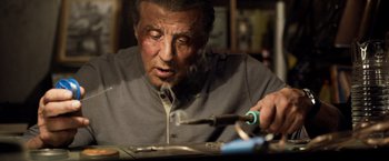Movie still from “Rambo: Last Blood” (2019), directed by Adrian Grunberg – Sylvester stallone working with a screwdriver on a piece of metal; Close Up shot, Low angle