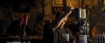 Movie still from “Rambo: Last Blood” (2019), directed by Adrian Grunberg – An older man sitting at a table in a dark room; Medium shot, Low angle