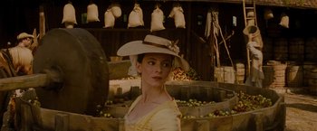 Movie still from “The Last of the Mohicans” (1992), directed by Michael Mann – A woman wearing a hat standing in front of apples; Medium shot, Over the shoulder angle