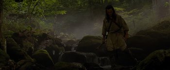 Movie still from “The Last of the Mohicans” (1992), directed by Michael Mann – A man dressed as a native american walking through a stream; Wide shot, Low angle