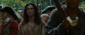 Movie still from “The Last of the Mohicans” (1992), directed by Michael Mann – A man with long black hair standing in front of a group of people; Medium shot, Over the shoulder angle
