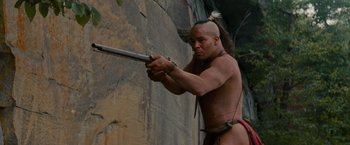 Movie still from “The Last of the Mohicans” (1992), directed by Michael Mann – A man in native american garb is holding a rifle; Medium shot, High angle