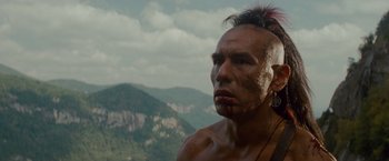Movie still from “The Last of the Mohicans” (1992), directed by Michael Mann – A man in native american garb looking into the distance; Close Up shot, Low angle