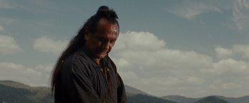 Movie still from “The Last of the Mohicans” (1992), directed by Michael Mann – A man with long black hair is standing in the mountains; Close Up shot, Low angle