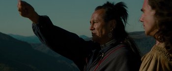 Movie still from “The Last of the Mohicans” (1992), directed by Michael Mann – A man with long black hair is holding his arm up; Close Up shot, Low angle