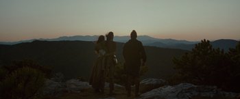Three people standing on top of a hill at dusk