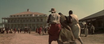 Movie still from “The League of Extraordinary Gentlemen” (2003), directed by Stephen Norrington – A group of people walking on the sand near a building; Extreme Wide shot, Low angle