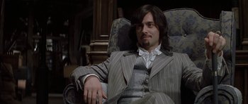 Movie still from “The League of Extraordinary Gentlemen” (2003), directed by Stephen Norrington – A man sitting in a chair wearing a suit and smoking a cigarette; Medium shot, High angle