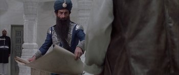 Movie still from “The League of Extraordinary Gentlemen” (2003), directed by Stephen Norrington – A man with a beard and a turban is pointing to something on a piece of paper in front of him; Medium shot, Low angle