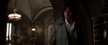 Movie still from “The League of Extraordinary Gentlemen” (2003), directed by Stephen Norrington – A man in a striped suit standing next to a wall; Medium shot, Over the shoulder angle