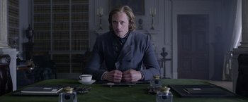 Movie still from “The Legend of Tarzan” (2016), directed by David Yates – A man sitting at a table in front of a cup of coffee; Medium shot, Over the shoulder angle