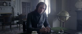Movie still from “The Legend of Tarzan” (2016), directed by David Yates – A man sitting at a table with a cup of coffee; Medium shot, Over the shoulder angle