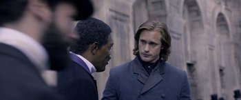 Movie still from “The Legend of Tarzan” (2016), directed by David Yates – Two men standing next to each other on a street; Medium shot, Over the shoulder angle