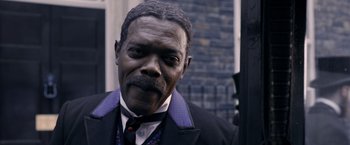 Movie still from “The Legend of Tarzan” (2016), directed by David Yates – An older man wearing a black suit and purple tie; Close Up shot, Over the shoulder angle