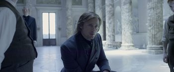 Movie still from “The Legend of Tarzan” (2016), directed by David Yates – A man in a suit sitting in front of pillars in a room; Medium shot, Low angle