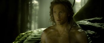 Movie still from “The Legend of Tarzan” (2016), directed by David Yates – A man with long hair and a bare torso is looking at the camera; Close Up shot, High angle