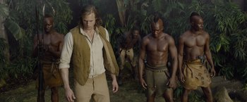 Movie still from “The Legend of Tarzan” (2016), directed by David Yates – A group of men standing next to each other in the woods; Medium shot, Over the shoulder angle