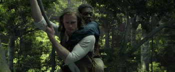Movie still from “The Legend of Tarzan” (2016), directed by David Yates – A man carrying a man on his back in the woods; Medium shot, High angle