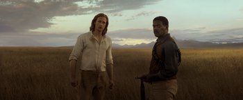 Movie still from “The Legend of Tarzan” (2016), directed by David Yates – Two men standing next to each other in a field; Medium shot, Over the shoulder angle