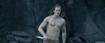 Movie still from “The Legend of Tarzan” (2016), directed by David Yates – A shirtless man holding a knife in his hand; Medium shot, Low angle