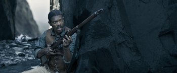 Movie still from “The Legend of Tarzan” (2016), directed by David Yates – A man holding a rifle in front of a rock wall; Close Up shot, High angle