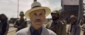 Movie still from “The Legend of Tarzan” (2016), directed by David Yates – A man in a suit and a hat is standing next to another man in a suit; Close Up shot, Low angle