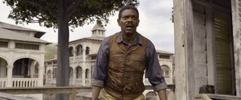 Movie still from “The Legend of Tarzan” (2016), directed by David Yates – A man in a brown vest standing in front of a building; Medium shot, Low angle