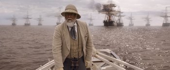 Movie still from “The Legend of Tarzan” (2016), directed by David Yates – An old man with a beard and a hat is standing on a boat; Medium shot, Over the shoulder angle