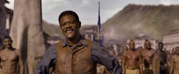 Movie still from “The Legend of Tarzan” (2016), directed by David Yates – A man in a brown vest standing in front of a group of people; Medium shot, Low angle