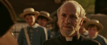 Movie still from “The Legend of Zorro” (2005), directed by Martin Campbell – An older man in a priest's outfit with other people in the background; Close Up shot, Over the shoulder angle