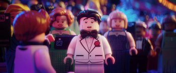 Movie still from “The Lego Batman Movie” (2017), directed by Chris McKay – A man in a suit and bow tie standing in front of a group of people; Extreme Close Up shot, Over the shoulder angle