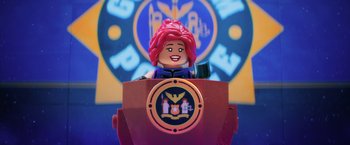 Movie still from “The Lego Batman Movie” (2017), directed by Chris McKay – A woman is sitting at a podium in front of a clock; Medium shot, Low angle