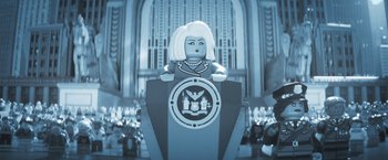 Movie still from “The Lego Batman Movie” (2017), directed by Chris McKay – A lego figure is sitting on top of a podium in front of a building; Close Up shot, Low angle