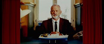Movie still from “The Life Aquatic with Steve Zissou” (2004), directed by Wes Anderson – An older man sitting at a table in front of a model ship; Medium shot, Low angle