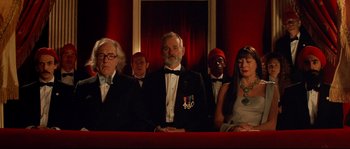 Movie still from “The Life Aquatic with Steve Zissou” (2004), directed by Wes Anderson – A group of men and a woman sitting in front of a red curtain; Medium shot, Low angle