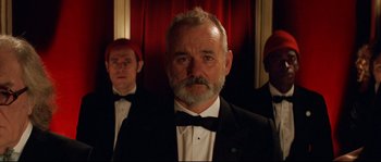Movie still from “The Life Aquatic with Steve Zissou” (2004), directed by Wes Anderson – A man in a suit and bow tie standing in front of two other men; Close Up shot, Low angle