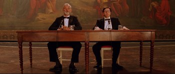Movie still from “The Life Aquatic with Steve Zissou” (2004), directed by Wes Anderson – A couple of men sitting in front of a wooden table; Wide shot, Low angle