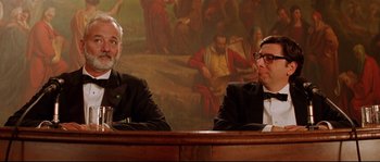 Movie still from “The Life Aquatic with Steve Zissou” (2004), directed by Wes Anderson – Two men in suits sitting in front of a painting; Medium shot, Over the shoulder angle
